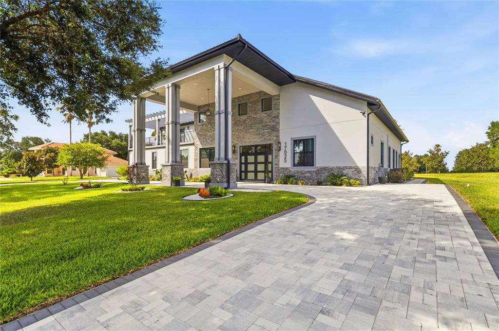 A modern house with a stone facade and a large covered porch faces a driveway — 17025 ROYAL PALM DRIVE, GROVELAND, FL