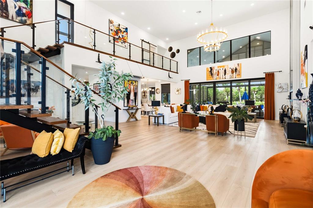 A spacious, modern living room features a floating staircase, high ceilings, and large glass doors — 17025 ROYAL PALM DRIVE, GROVELAND, FL