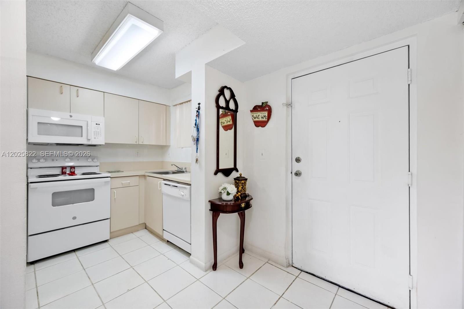 A kitchen features white appliances, light-colored cabinets, and tile flooring next to an entry door — 14951 SW 82nd Ln # 403, Miami FL 33193, MIAMI, FL