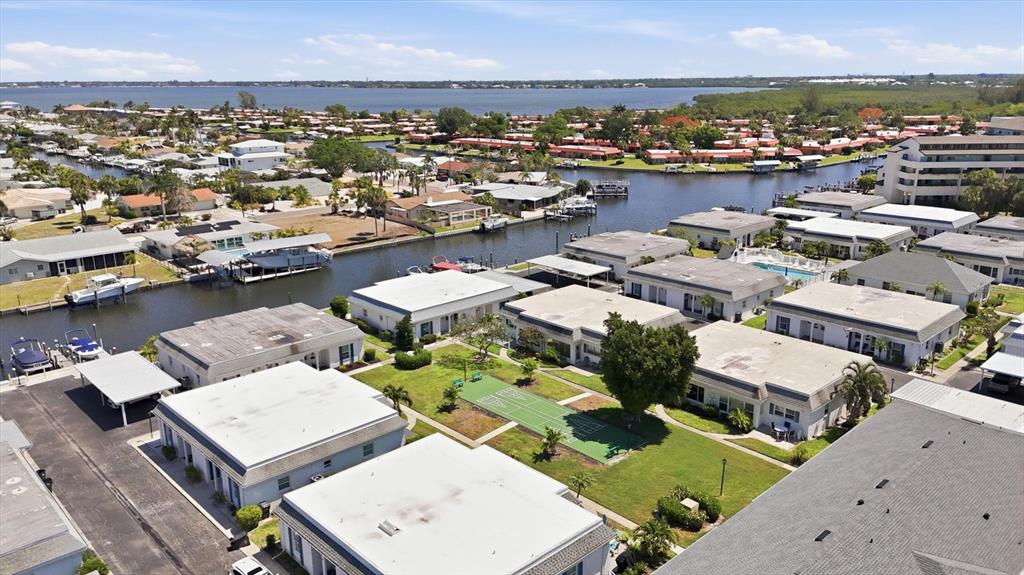 An aerial view shows a waterfront residential complex with flat-roofed buildings and a shuffleboard court — 9914 SEBASTIAN COURT, BRADENTON, FL