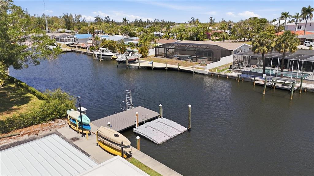 An aerial view shows a canal with boat docks, kayaks, and waterfront homes with pools — 9914 SEBASTIAN COURT, BRADENTON, FL