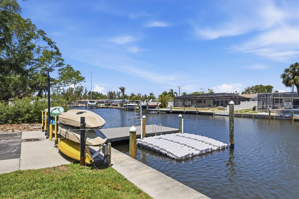 A canal-side dock features a kayak rack, a floating platform, and nearby residential homes — 9914 SEBASTIAN COURT, BRADENTON, FL