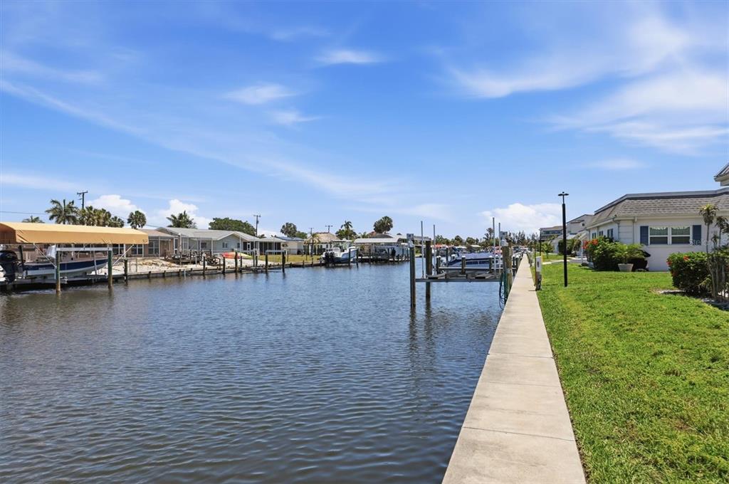 A canal view showing boat docks, residential houses, and a concrete walkway along the grass — 9914 SEBASTIAN COURT, BRADENTON, FL