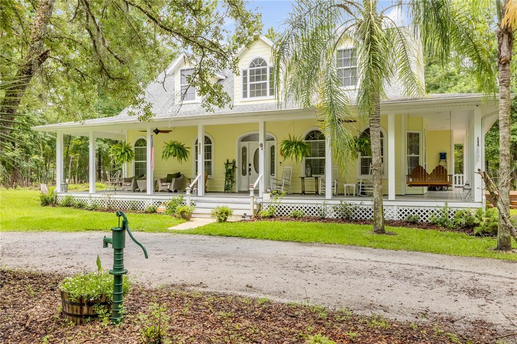 A yellow two-story house with a large wrap-around porch and a front yard pump — 227 N SAMSULA DRIVE, NEW SMYRNA BEACH, FL