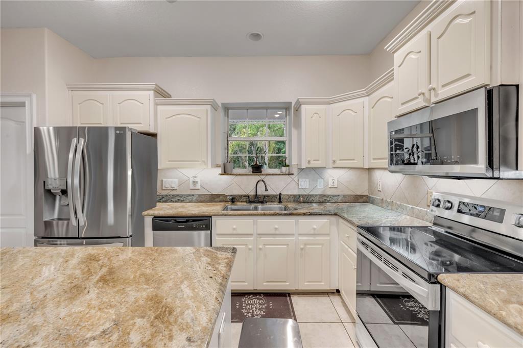 A kitchen features cream-colored cabinets, granite countertops, stainless steel appliances, and a central island — 227 N SAMSULA DRIVE, NEW SMYRNA BEACH, FL