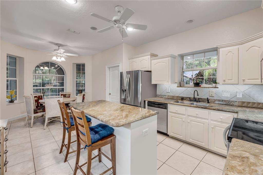 A kitchen features white cabinetry, granite countertops, a center island with stools, and tile flooring — 227 N SAMSULA DRIVE, NEW SMYRNA BEACH, FL