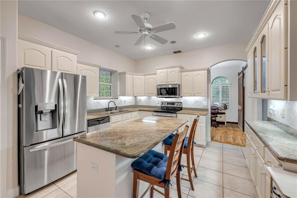 A kitchen features cream cabinets, granite countertops, stainless steel appliances, and a central island — 227 N SAMSULA DRIVE, NEW SMYRNA BEACH, FL