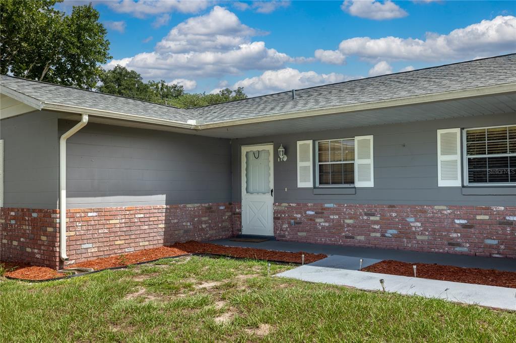The exterior of a single-story house features gray siding, a brick base, and a white door — 1868 NE 29TH STREET, OCALA, FL