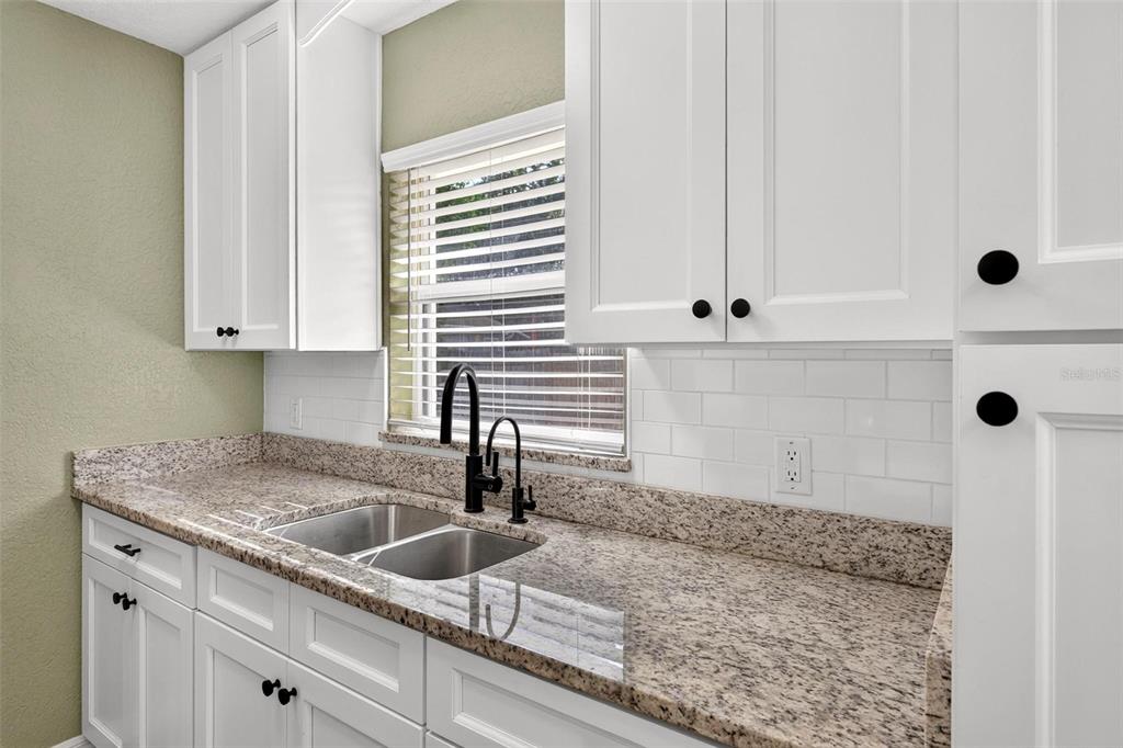 A kitchen features white cabinets, granite countertops, a double sink, and a subway tile backsplash — 1125 N TREMAIN STREET, MOUNT DORA, FL