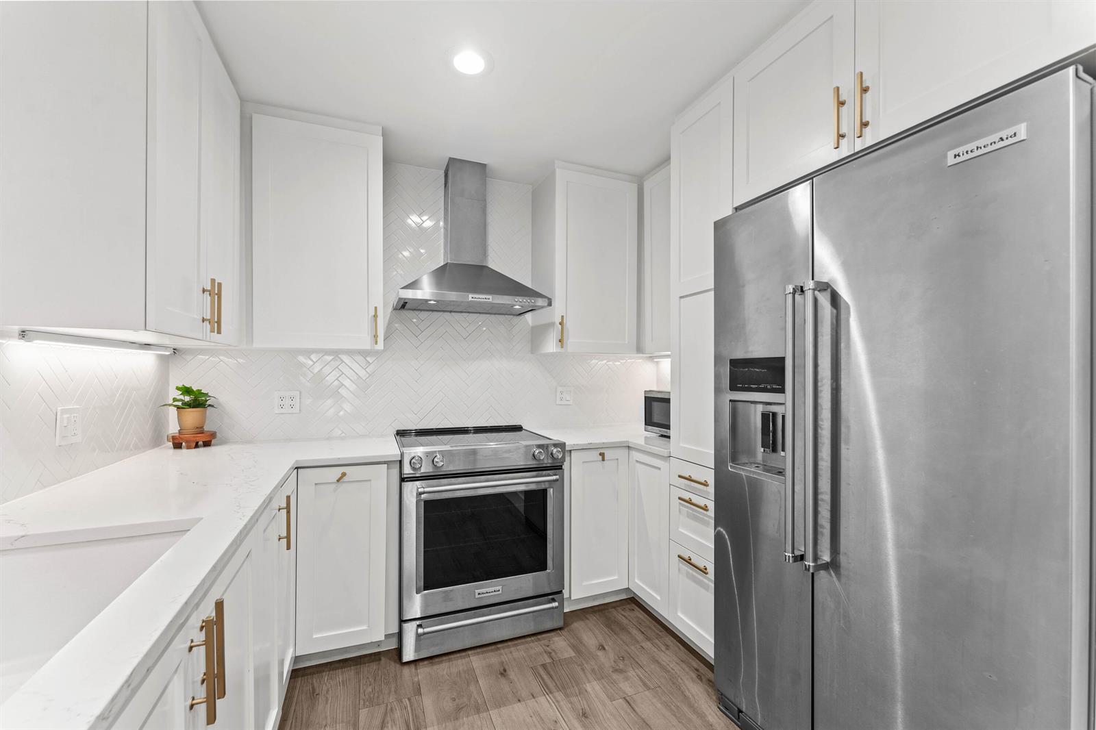 A modern kitchen features white cabinets, stainless steel appliances, a herringbone tile backsplash, and wood flooring — 250 S Ocean Boulevard # 279, Delray Beach FL 33483, DELRAY BEACH, FL