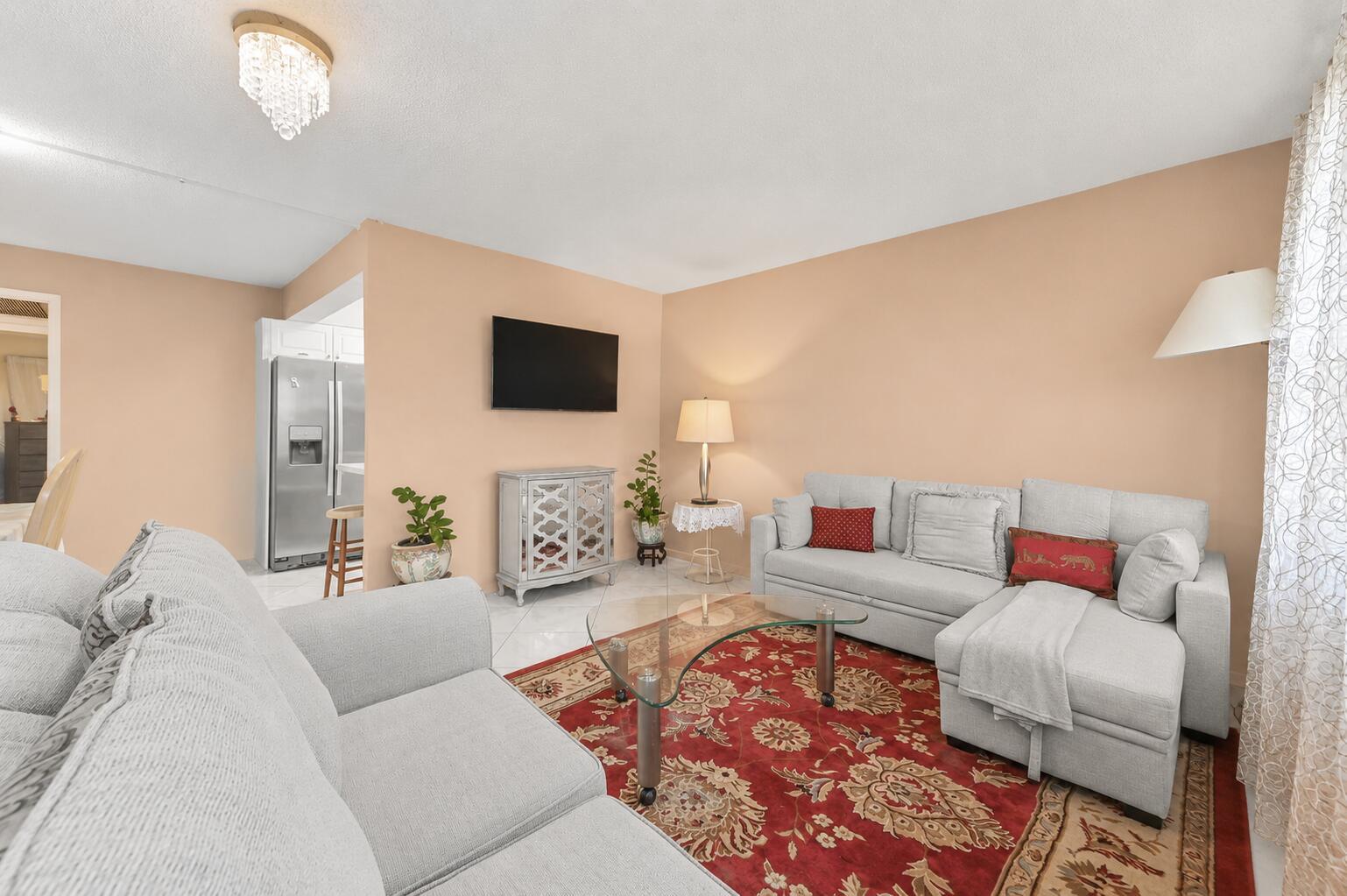 A living room features a grey sectional sofa, a red patterned rug, and a television — 1069 Cornwall D, Boca Raton FL 33434, BOCA RATON, FL