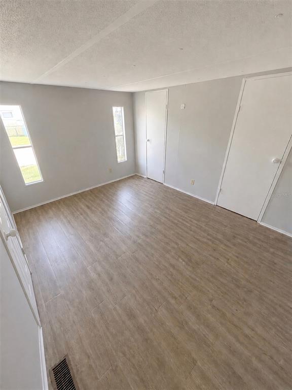 An empty room features light wood-look flooring, gray walls, two windows, and two white doors — 35 SUNSET CIRCLE, LAKE ALFRED, FL