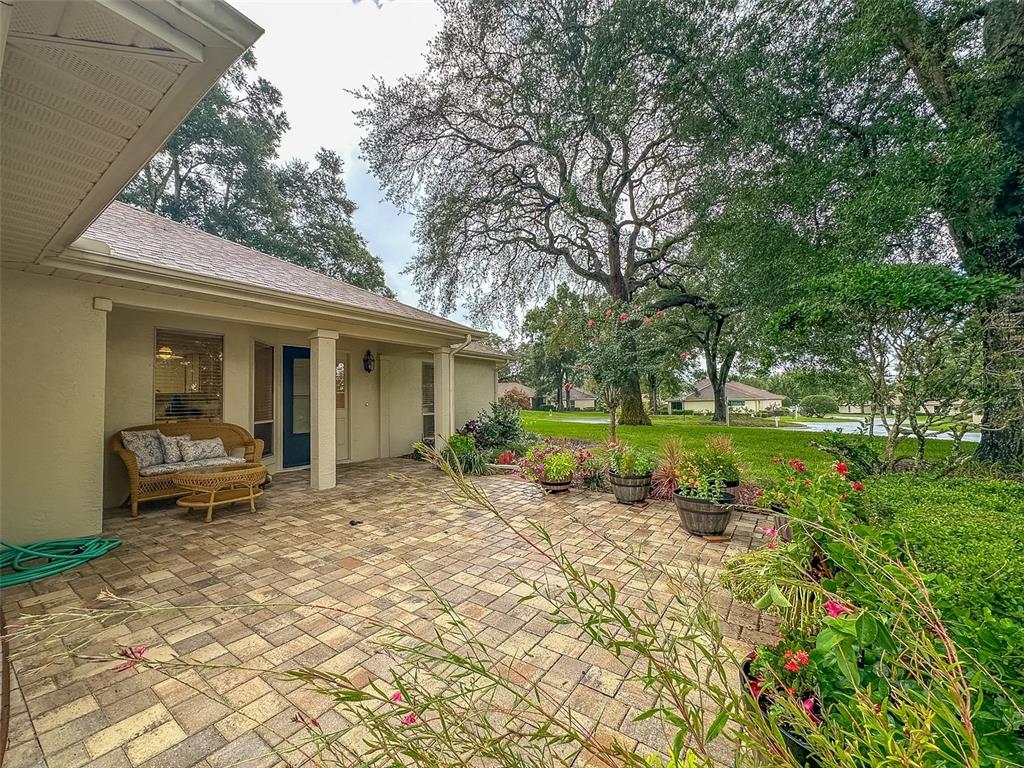 A paved patio features a wicker loveseat and potted plants under a covered porch — 5941 W DEDHAM TRAIL, CRYSTAL RIVER, FL