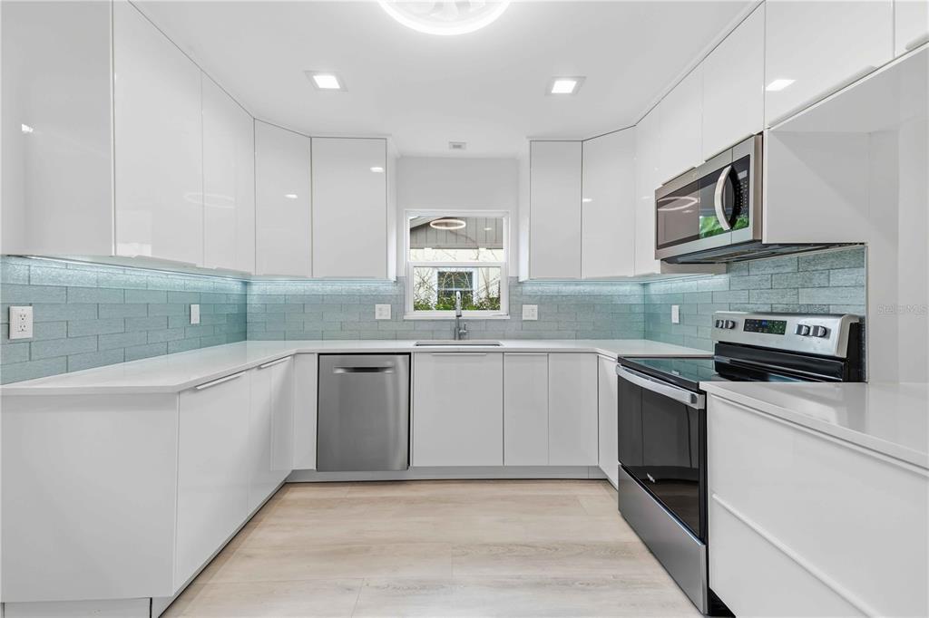 A modern kitchen features white flat-panel cabinets, stainless steel appliances, and a blue subway tile backsplash — 4756 OAK HILL DRIVE UNIT 16, SARASOTA, FL