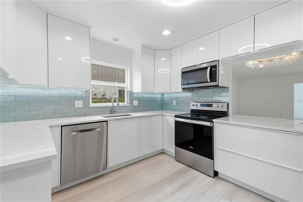 A modern kitchen features white glossy cabinets, stainless steel appliances, and a light blue backsplash — 4756 OAK HILL DRIVE UNIT 16, SARASOTA, FL