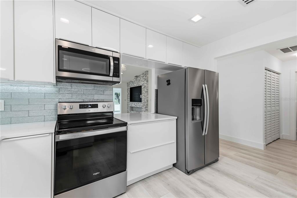 A modern kitchen features white glossy cabinets, stainless steel appliances, and a light blue backsplash — 4756 OAK HILL DRIVE UNIT 16, SARASOTA, FL