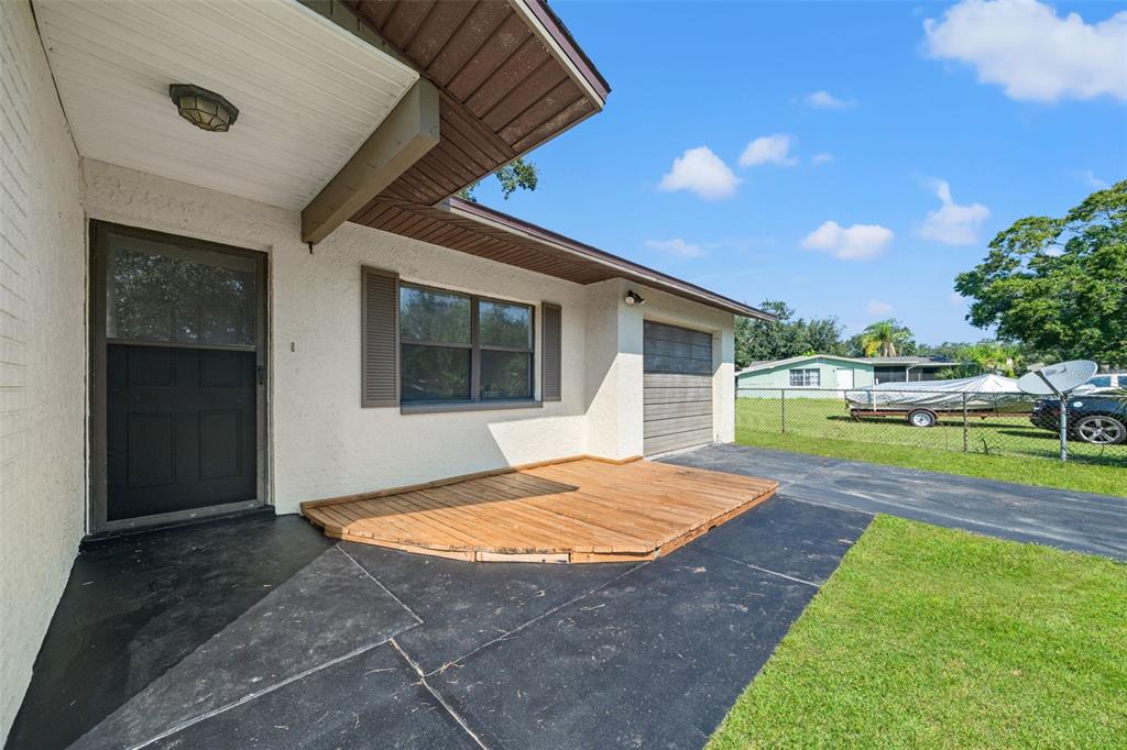 A house exterior features a black front door, a wooden deck, and a garage — 5828 MARIPOSA DRIVE, HOLIDAY, FL