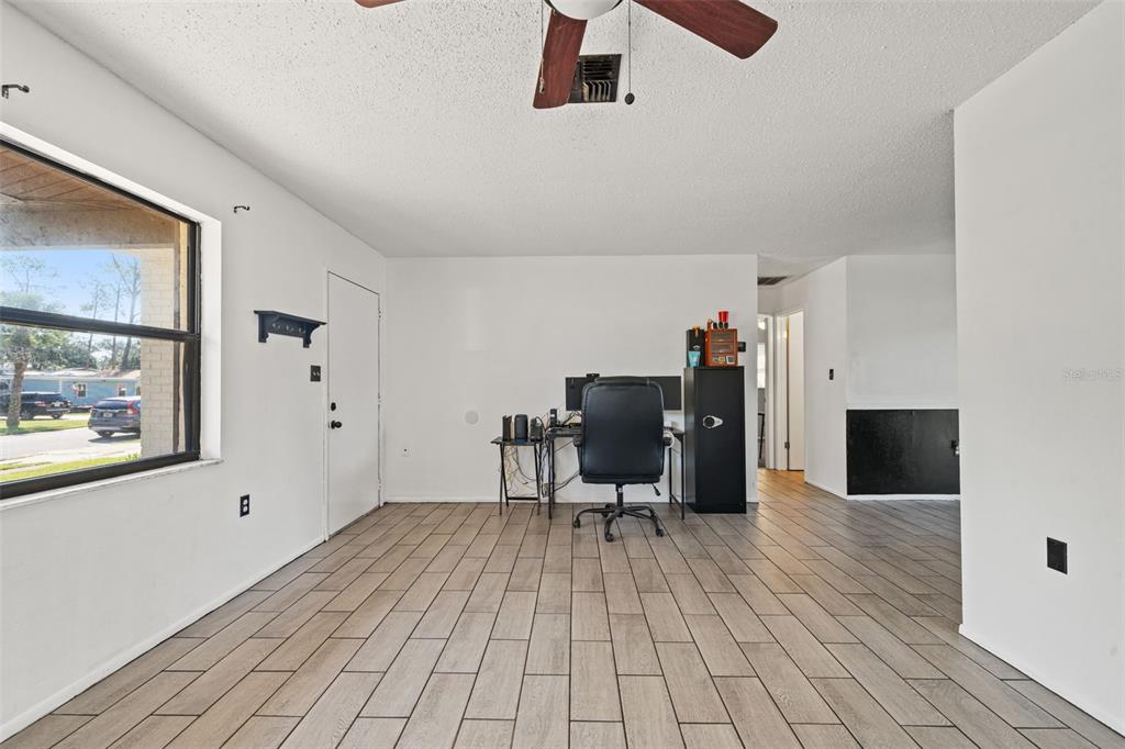 A bright room features light wood-look tile flooring, a ceiling fan, and a home office setup — 5828 MARIPOSA DRIVE, HOLIDAY, FL