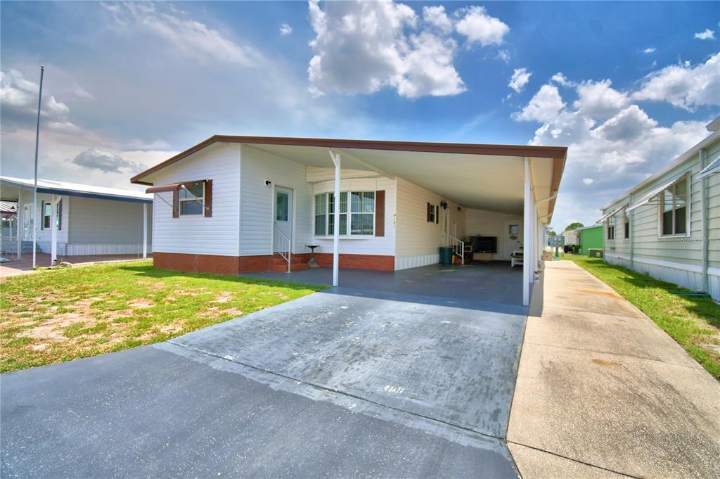 A single-story manufactured home with white siding, a brick base, and an attached carport — 4242 CEDARWOOD STREET, WINTER HAVEN, FL