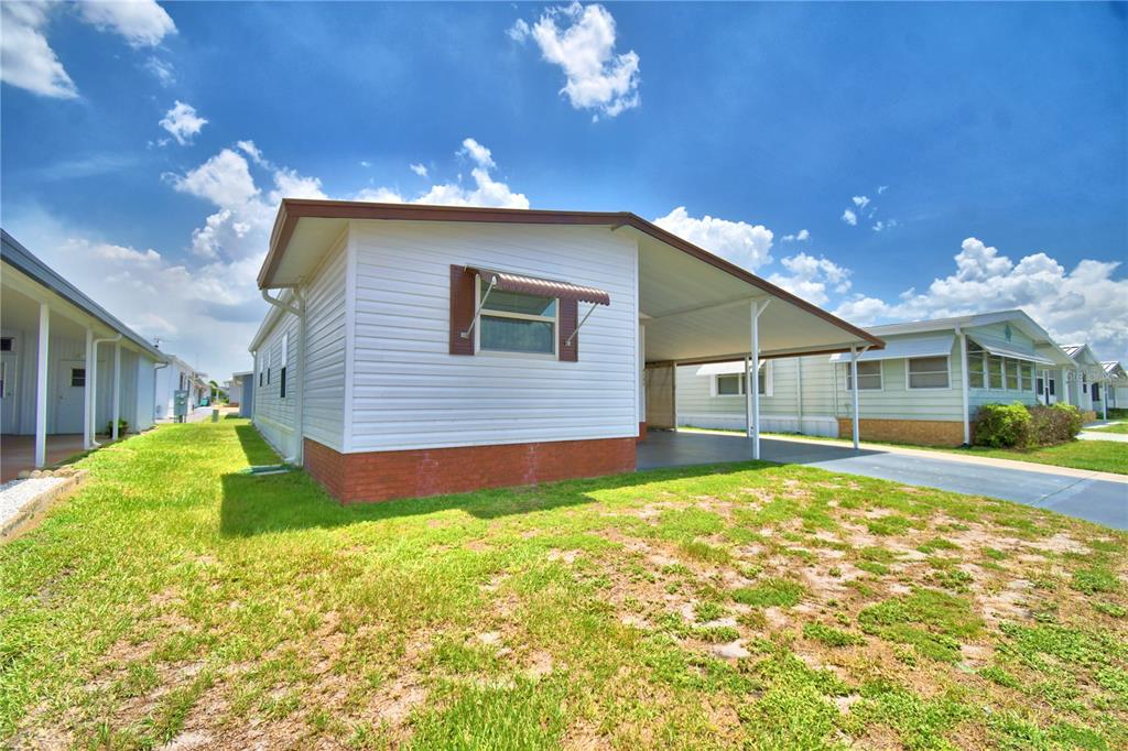 A white mobile home with a brick base, a side carport, and a grassy yard — 4242 CEDARWOOD STREET, WINTER HAVEN, FL