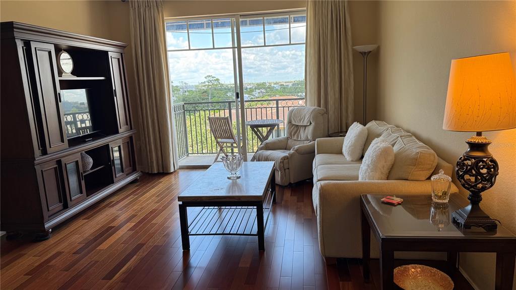 A living room features hardwood floors, a large entertainment center, a sofa, and a balcony view — 1064 N TAMIAMI TRAIL UNIT 1635, SARASOTA, FL