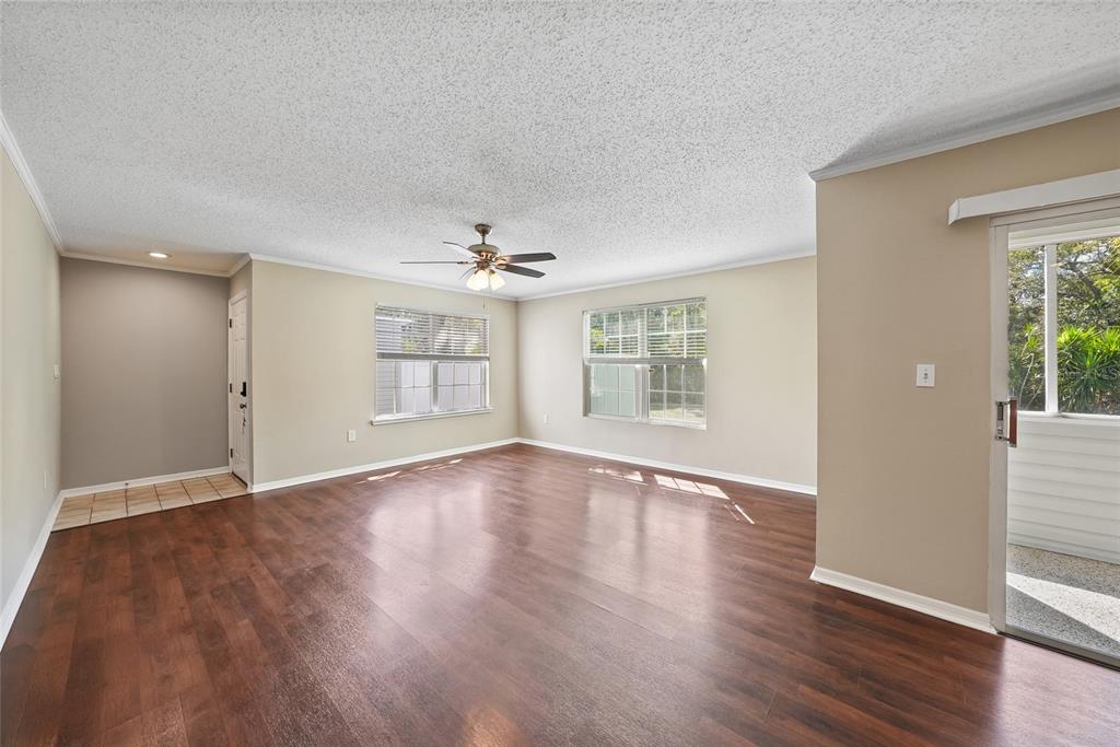 An empty living room features dark wood-look flooring, beige walls, and a ceiling fan — 8350 SAVANNAH TRACE CIRCLE UNIT 1703, TAMPA, FL