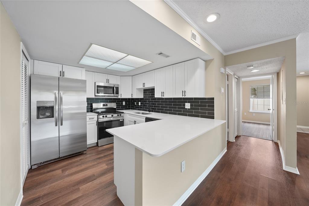 A kitchen with white cabinets, stainless steel appliances, a dark tile backsplash, and wood flooring — 8350 SAVANNAH TRACE CIRCLE UNIT 1703, TAMPA, FL