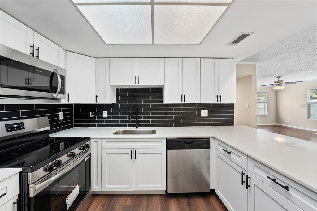 A kitchen features white cabinets, black subway tile backsplash, stainless steel appliances, and quartz countertops — 8350 SAVANNAH TRACE CIRCLE UNIT 1703, TAMPA, FL