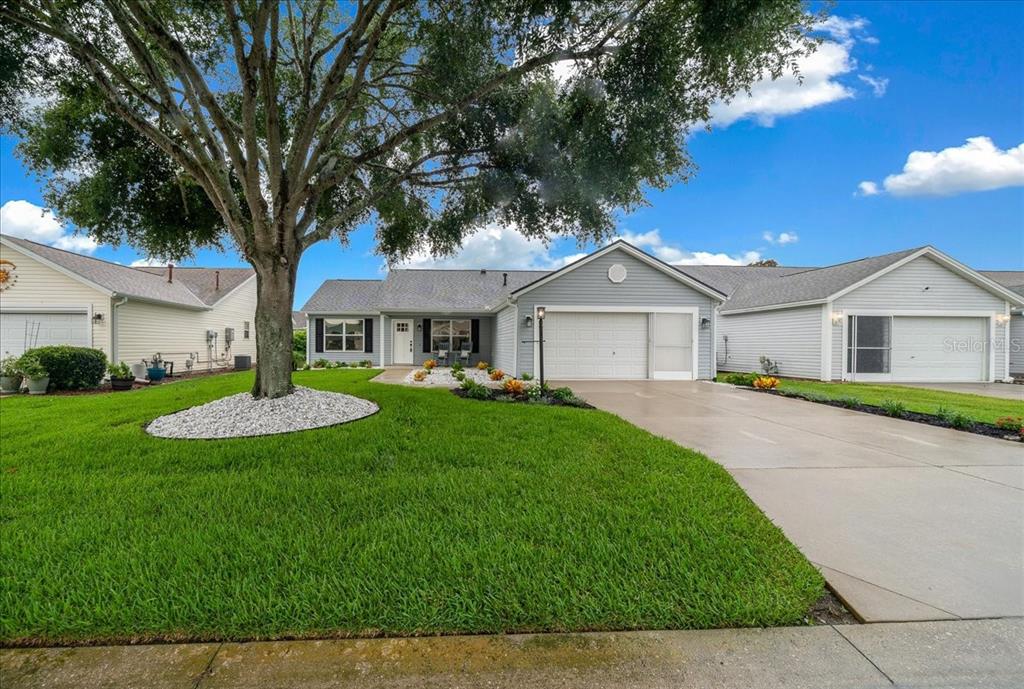 A single-story house with light blue siding, a two-car garage, and a large front tree — 3048 GLENWOOD PLACE, THE VILLAGES, FL