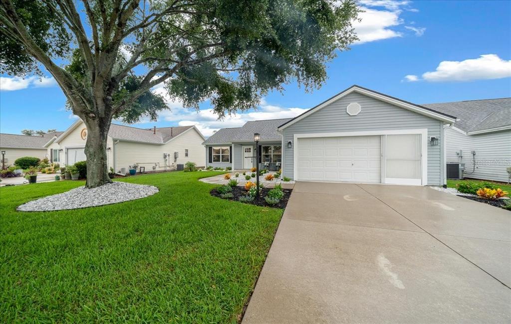 A single-story house with light blue siding, a two-car garage, and a large front tree — 3048 GLENWOOD PLACE, THE VILLAGES, FL