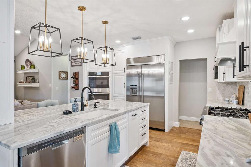 A modern kitchen features white cabinets, marble countertops, stainless steel appliances, and three pendant lights — 4571 KAWILLA CREST PLACE, WINTER PARK, FL