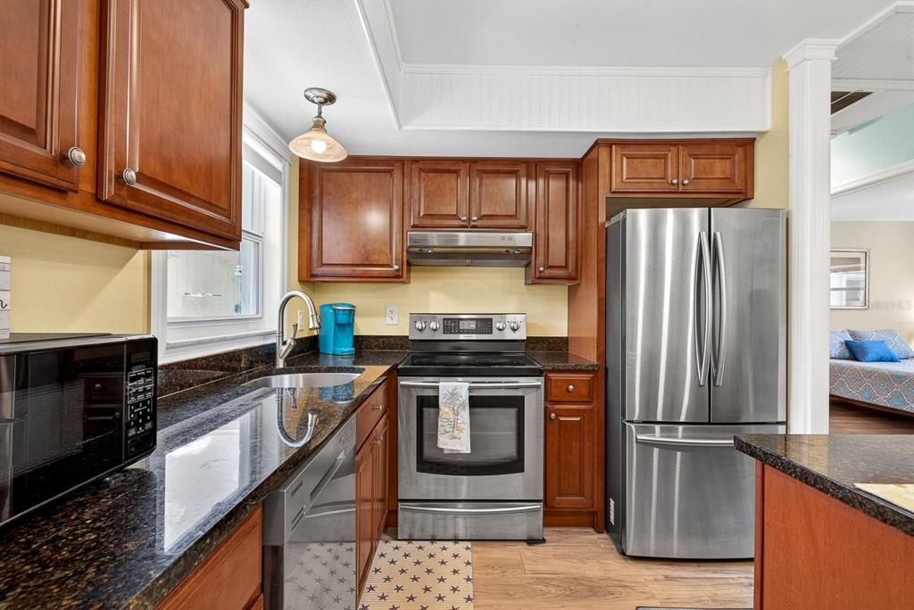 A kitchen features wood cabinets, dark granite countertops, stainless steel appliances, and light wood flooring — 5055 LIVE OAK CIRCLE UNIT 5055, BRADENTON, FL