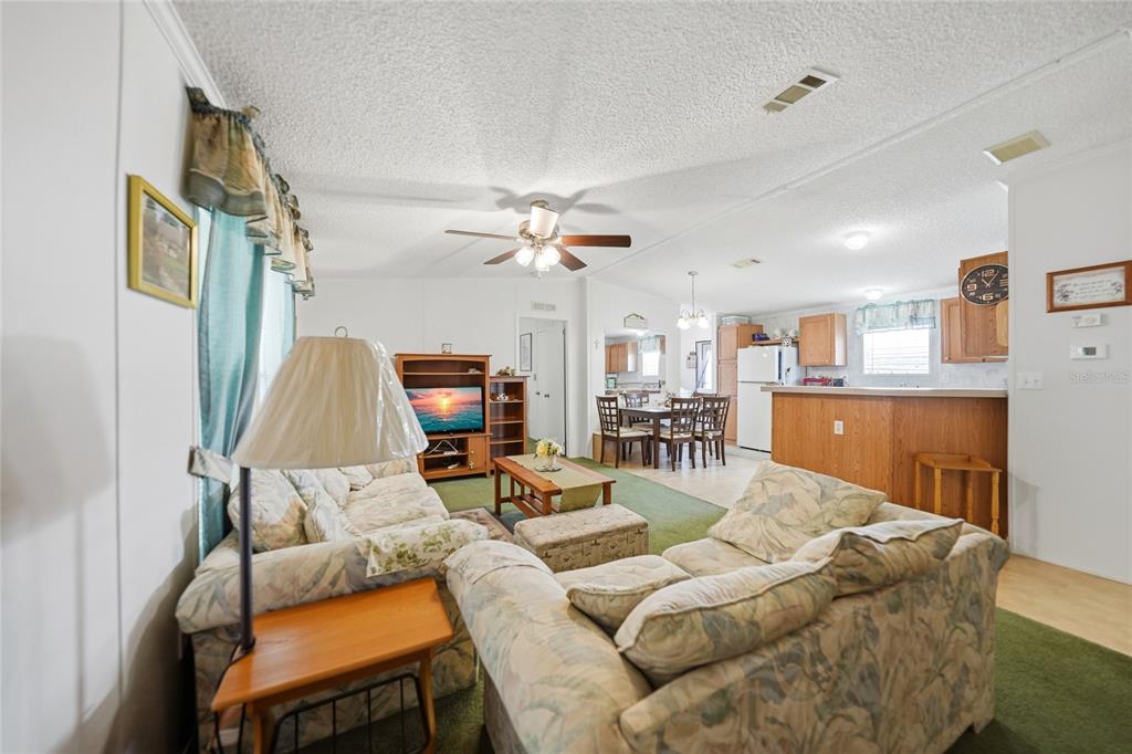 A living room with floral sofas, a green carpet, and an open kitchen in the background — 10303 BURNT STORE ROAD UNIT 35, PUNTA GORDA, FL
