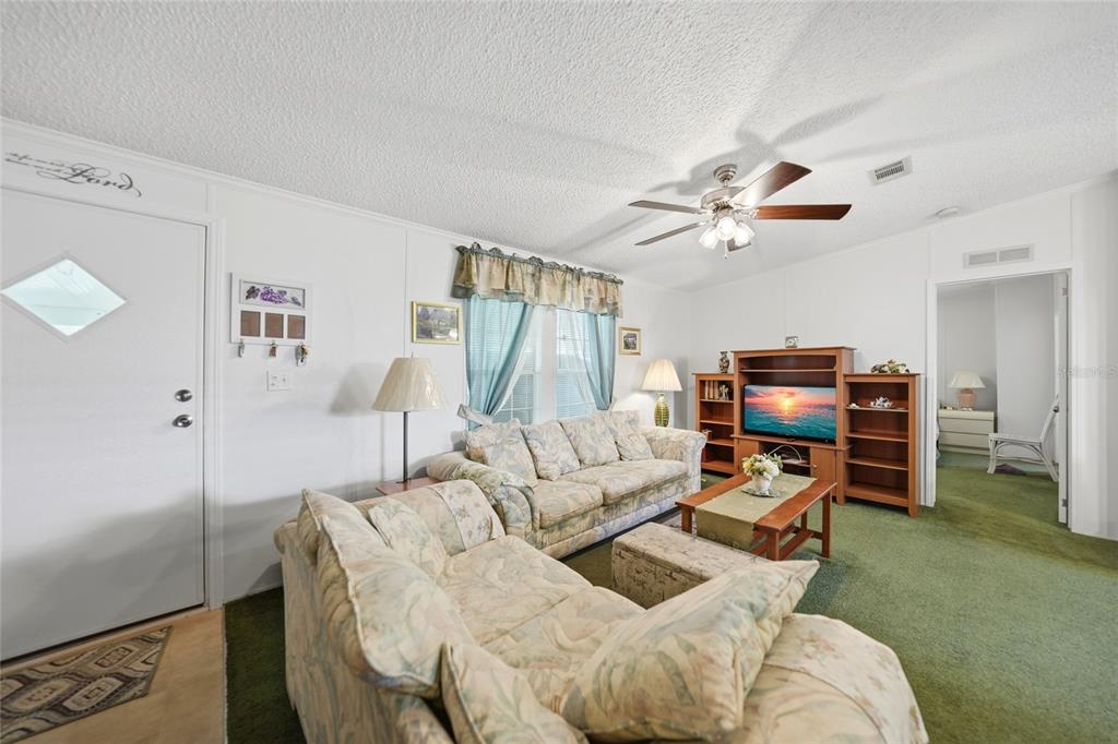 A living room features floral sofas, a wooden entertainment center, and green carpeting — 10303 BURNT STORE ROAD UNIT 35, PUNTA GORDA, FL
