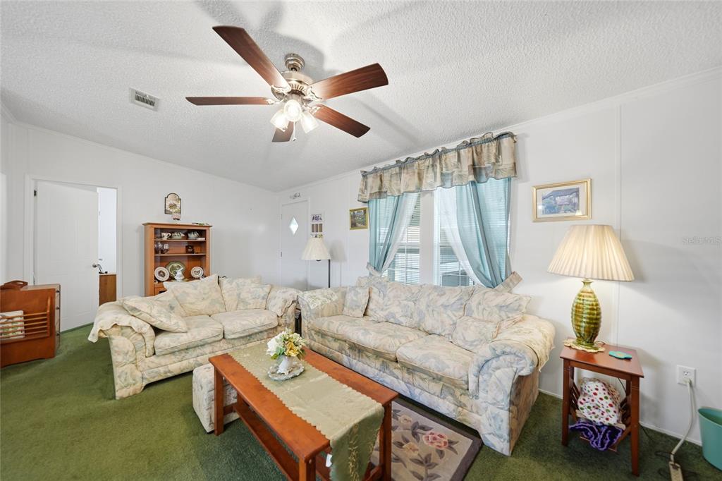 A living room features green carpeting, two floral sofas, a wooden coffee table, and ceiling fan — 10303 BURNT STORE ROAD UNIT 35, PUNTA GORDA, FL