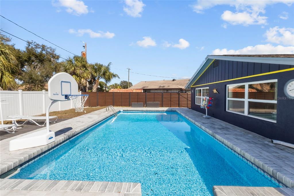 A rectangular swimming pool sits in a backyard next to a dark blue house exterior — 3340 SUNSET BEACH DRIVE, VENICE, FL