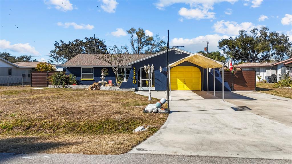 A blue house with a yellow garage door and a white carport stands on grass — 3340 SUNSET BEACH DRIVE, VENICE, FL