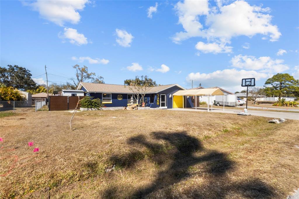 A blue single-story house features a yellow front door, a carport, and a large yard — 3340 SUNSET BEACH DRIVE, VENICE, FL