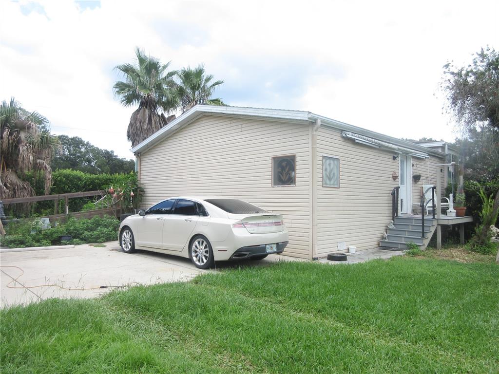 A beige mobile home with a parked sedan in the driveway and a small wooden deck — 16000 N HWY 329, REDDICK, FL