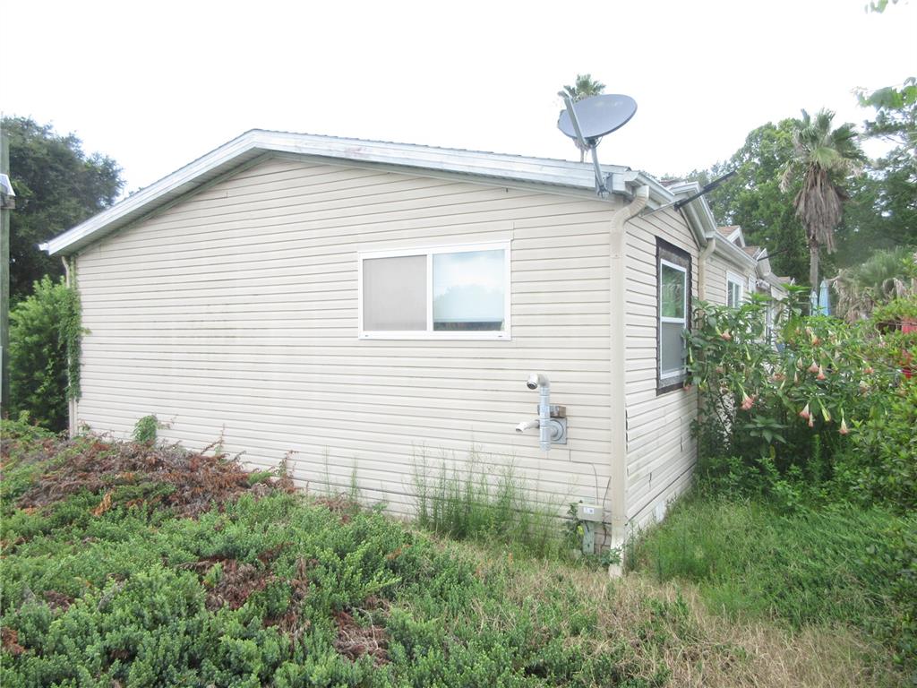 The exterior side of a tan vinyl-sided house features a window and a satellite dish — 16000 N HWY 329, REDDICK, FL