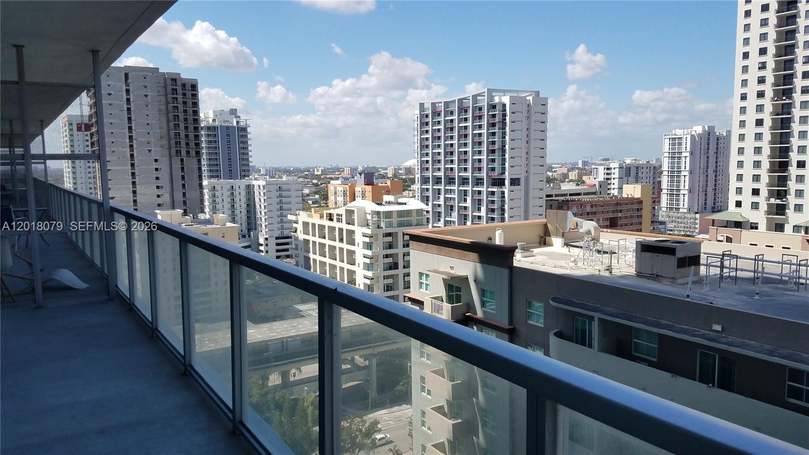 A high-rise balcony overlooks a dense urban cityscape with multiple apartment buildings under a blue sky — 1111 SW 1st Ave, Miami FL 33130, MIAMI, FL