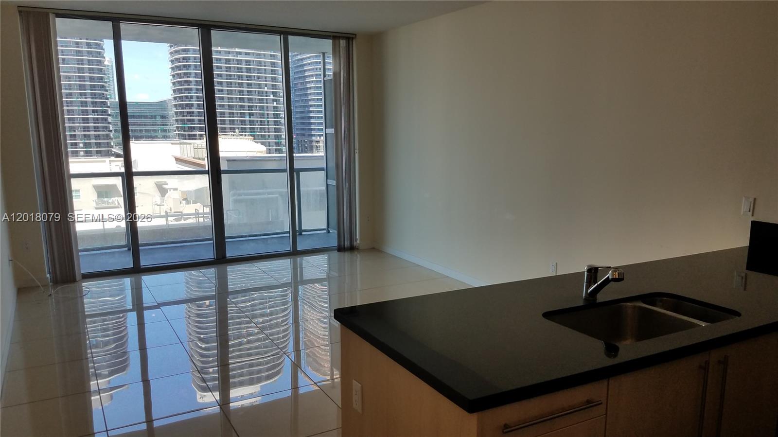 A kitchen island with a dark countertop overlooks a living area with floor-to-ceiling windows — 1111 SW 1st Ave, Miami FL 33130, MIAMI, FL