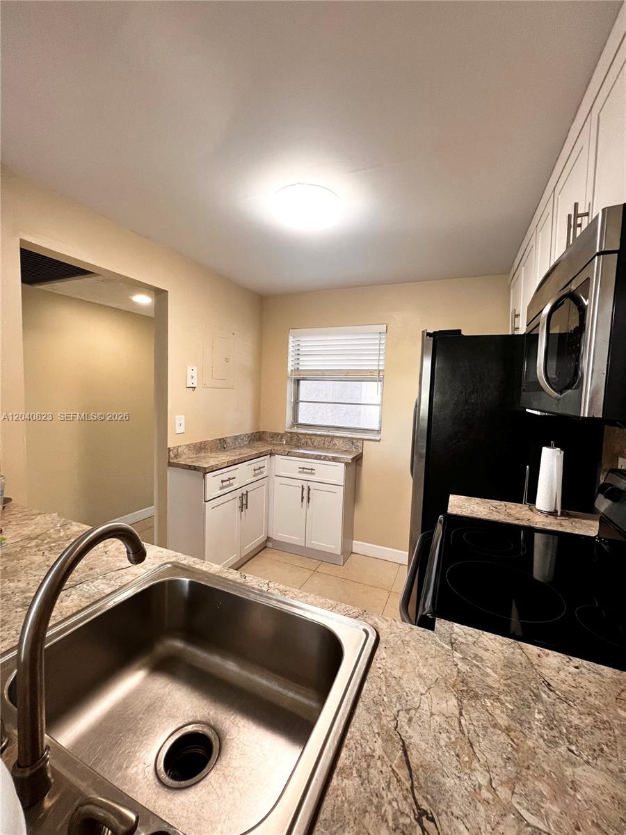 A kitchen features white cabinets, granite countertops, a stainless steel sink, and black appliances — 9235 Lagoon Pl # 109, Davie FL 33324, DAVIE, FL