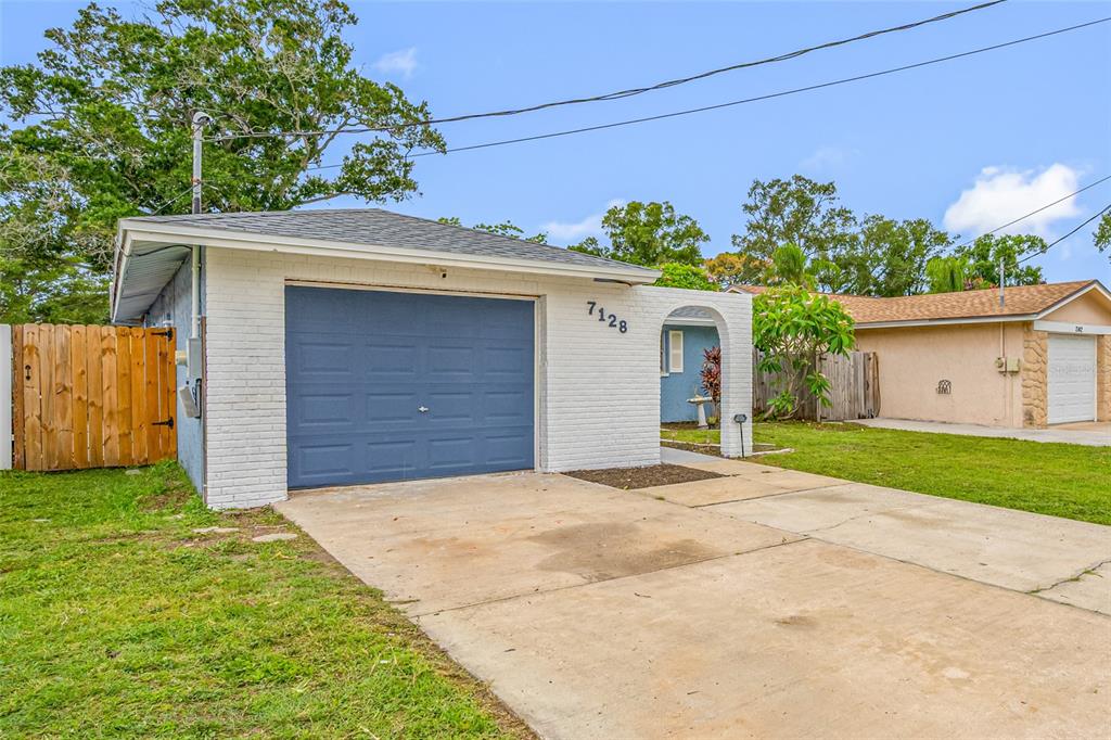 A white brick house features a blue garage door and a covered entryway — 7128 64TH WAY N, PINELLAS PARK, FL