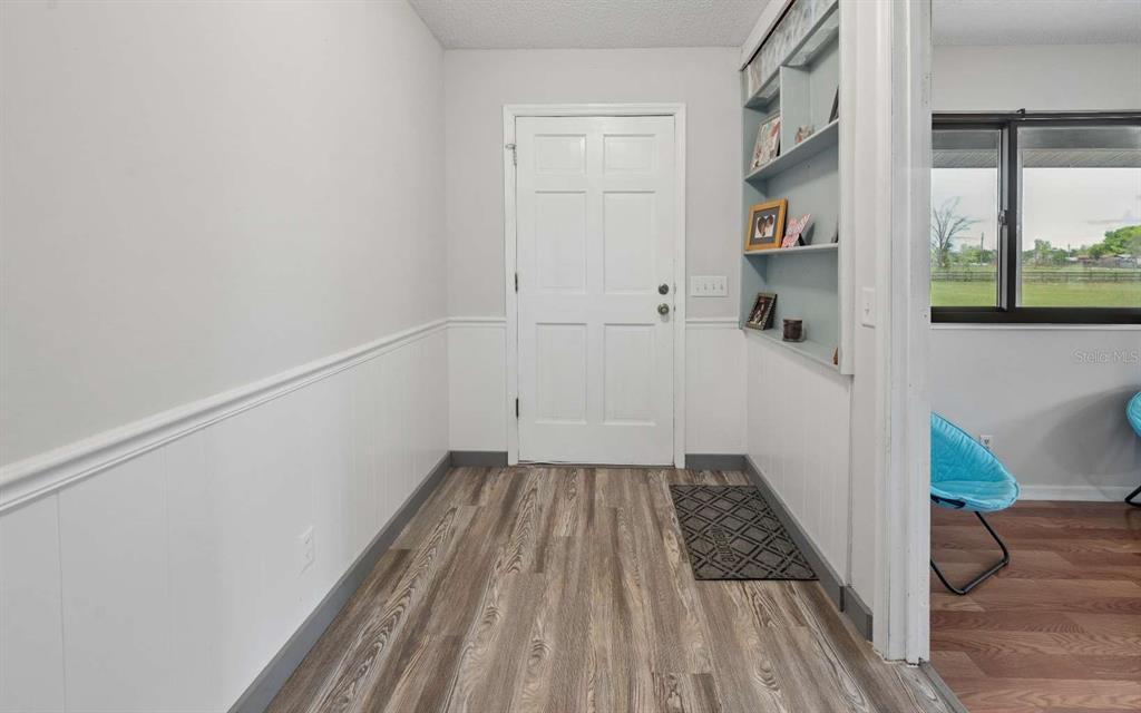 An entryway features wood-look flooring, white wainscoting, a white door, and built-in wall shelving — 3582 210TH PATH, LAKE CITY, FL