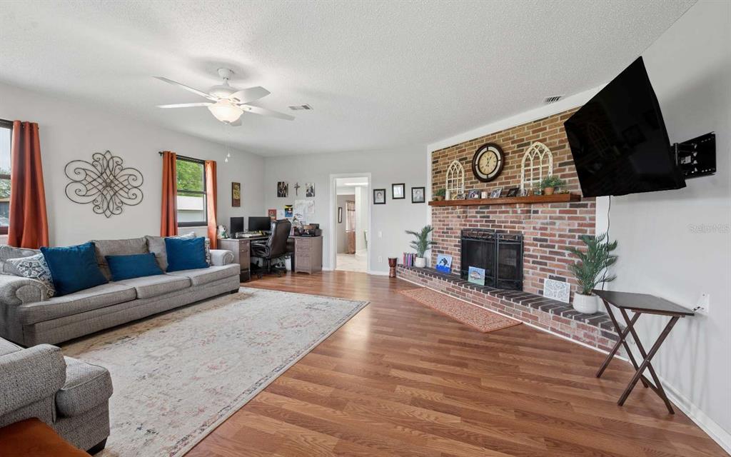 A living room features a brick fireplace, wood-look flooring, a ceiling fan, and a sofa — 3582 210TH PATH, LAKE CITY, FL