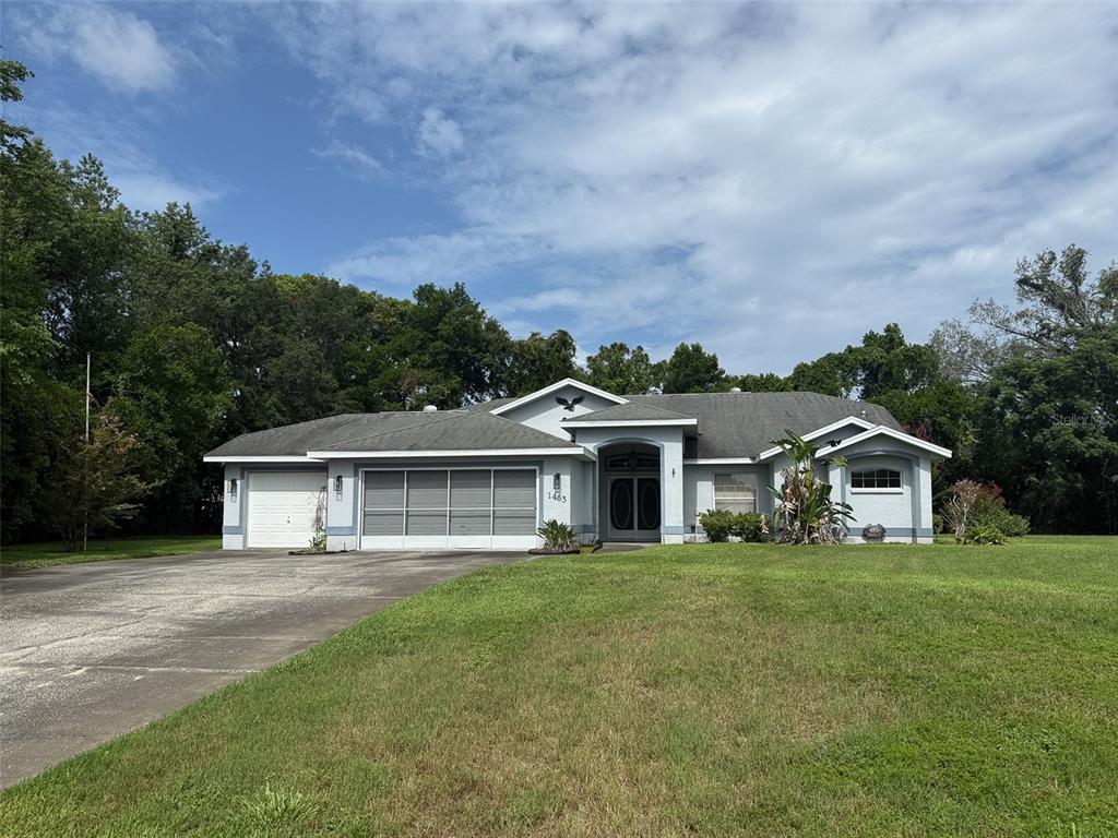 A single-story house with a gray roof, light blue exterior, and a large concrete driveway — 1463 BRIGADIER DRIVE, SPRING HILL, FL