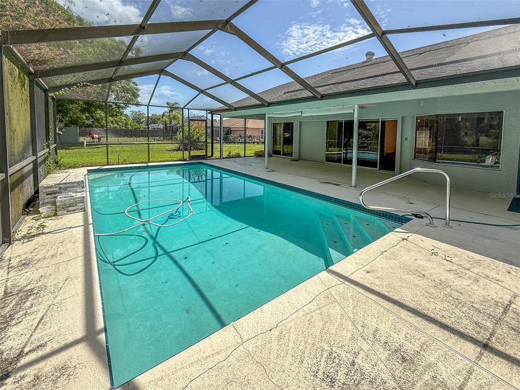 A swimming pool with a screen enclosure sits on a concrete patio behind a house — 1463 BRIGADIER DRIVE, SPRING HILL, FL