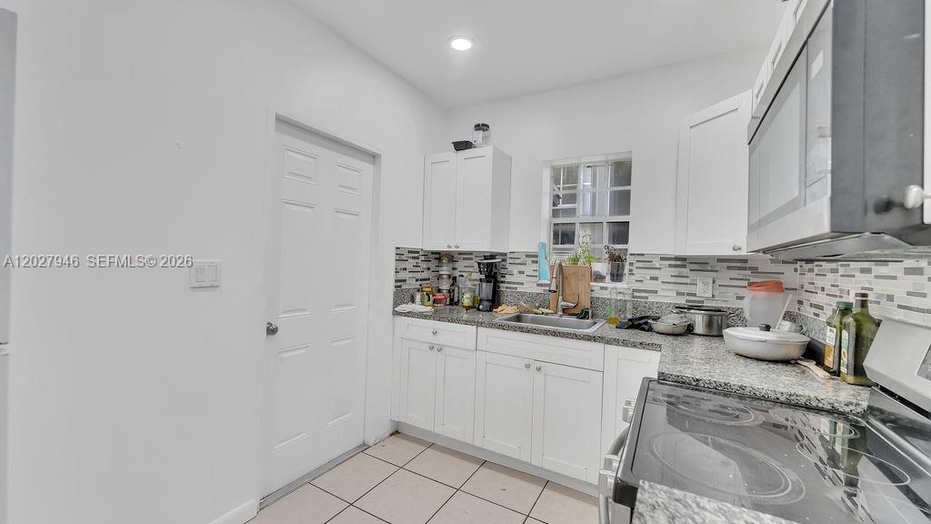A kitchen features white cabinets, granite countertops, a tiled backsplash, and stainless steel appliances — 242 SW 15th Ave, Miami FL 33135, MIAMI, FL
