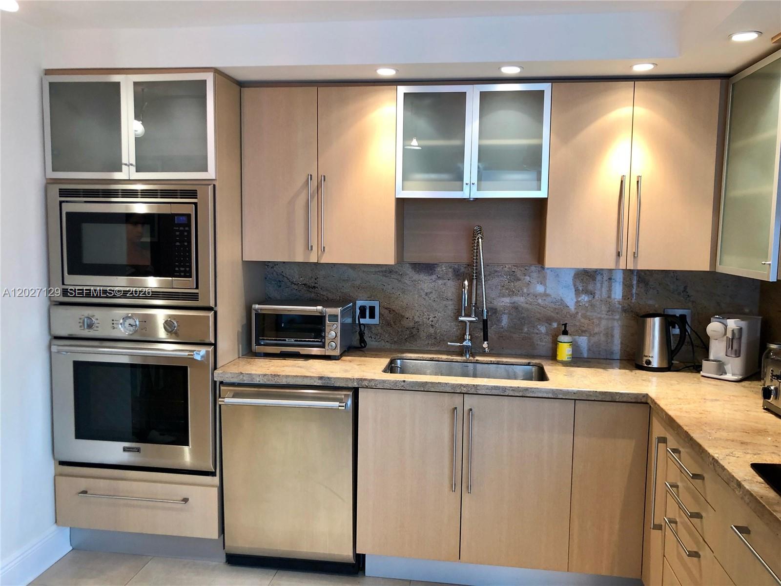 A kitchen features light wood cabinets, stainless steel appliances, and a stone countertop and backsplash — 607 Ocean Dr # 9K, Key Biscayne FL 33149, KEY BISCAYNE, FL